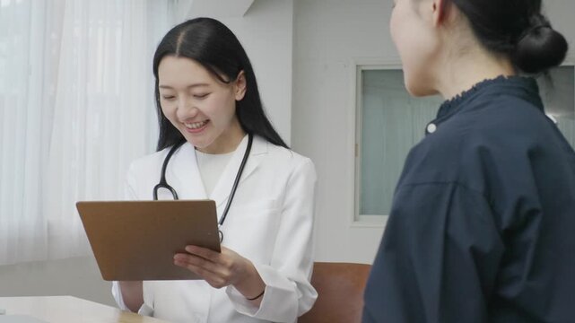 Young Japanese female doctor writing on medical chart during patient examination