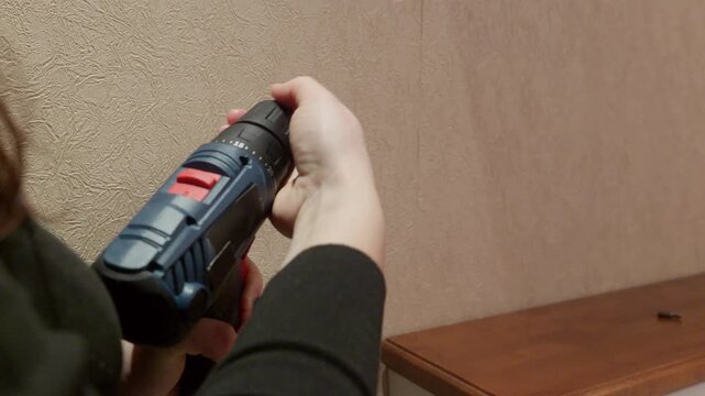 Hand gripping compact cordless screwdriver against textured beige wall, showcasing handheld power tool for home repairs, maintenance tasks, includes high quality original audio.