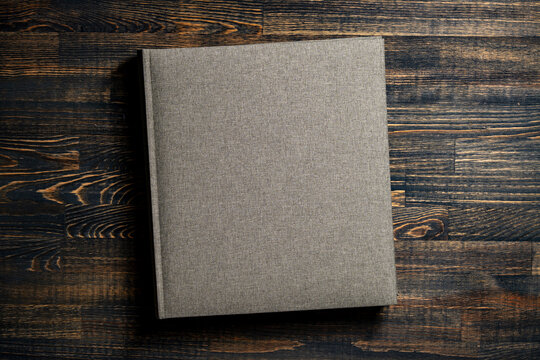 Blank linen book cover mock up on wooden table. Top view of grey fabric notebook photo album or book with hard linen cover template on textured dark wooden table with dramatic lighting copy space