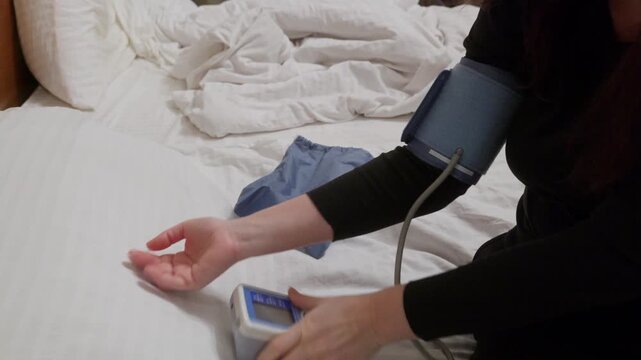 Healthcare professional takes blood pressure reading using electronic monitor with inflatable cuff on patient arm in home setting.