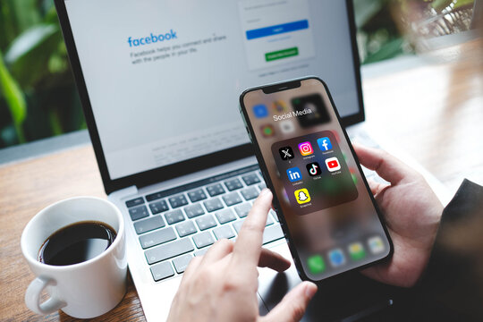 Bangkok, Thailand. July 26, 2026; A person holds a smartphone displaying popular social media app icons in front of a laptop.