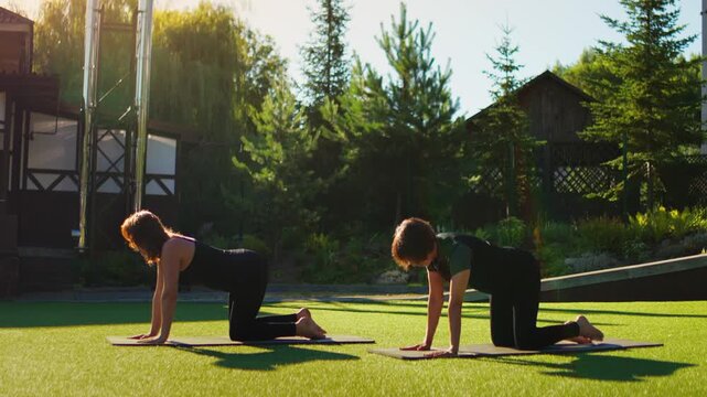 Slow motion Pilates sequence with two elderly women practicing outdoor balance and core strengthening exercises together on yoga mats in a peaceful garden setting