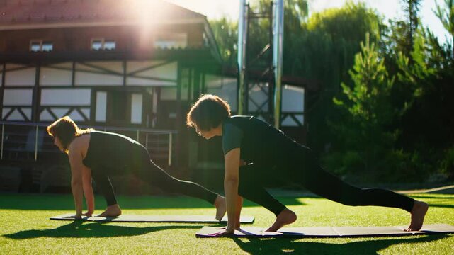 Elderly women practicing slow motion Pilates lunges together outdoors on yoga mats, improving balance, strength, and flexibility under warm natural sunlight