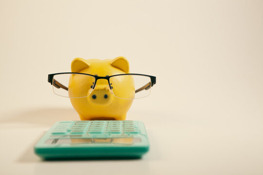 Piggy bank with eyeglasses and calculator on white background