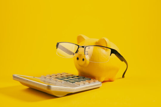 Piggy bank with eyeglasses and calculator on yellow background