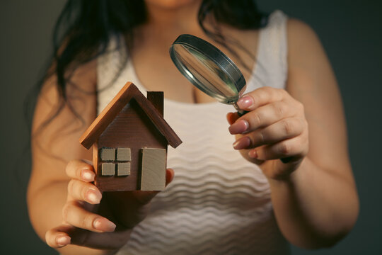 Woman looking at house model through a magnifying glass on gray background