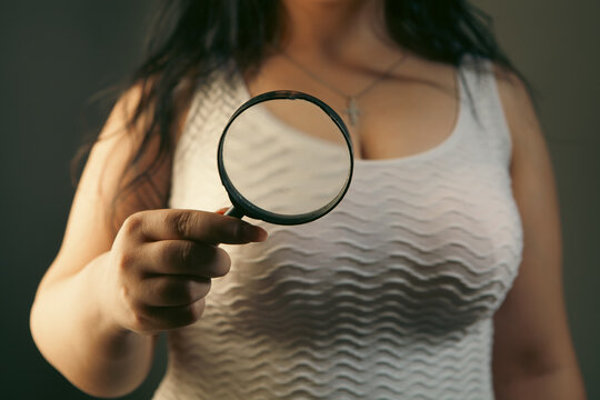 Young woman holding a magnifying glass. Focus on the magnifier