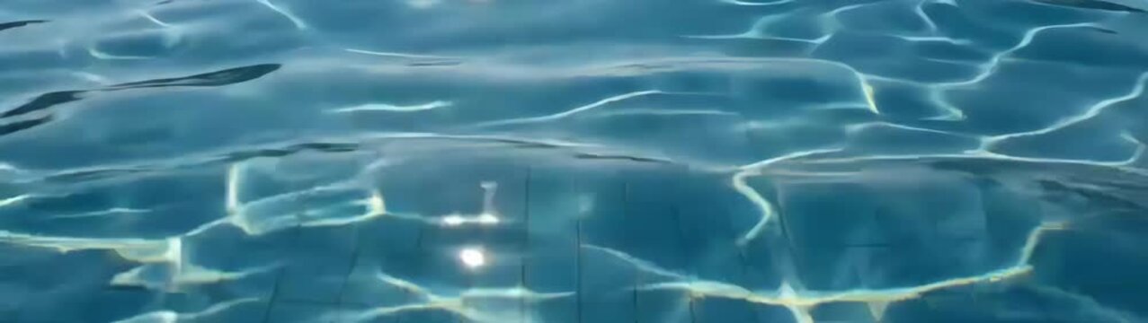Swimming pool surface with shimmering sunlight reflections Clean pool tiles visible under the gently undulating expanse.
