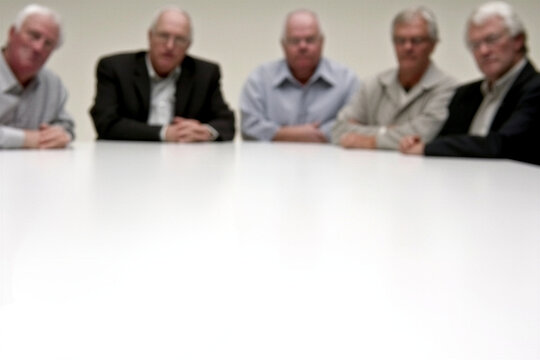 Blurred row of senior men at a white boardroom table