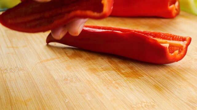 A close-up view of a chef slicing a ripe red bell pepper into neat, even pieces on a wooden cutting board for a healthy home-cooking recipe and culinary video project.