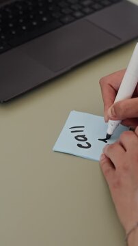 Vertical video of young adult woman writing reminder on sticky note and pinning it to corkboard. Footage is perfect for time management and office productivity marketing