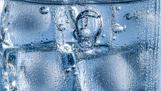 Refreshing clear ice cubes floating inside cold glass with condensation droplets and sparkling blue water bubbles