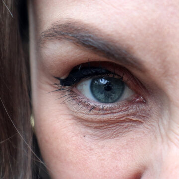 Dettaglio ravvicinato in primo piano di un occhio azzurro femminile con trucco eyeliner nero e rughe d'espressione sulla pelle matura