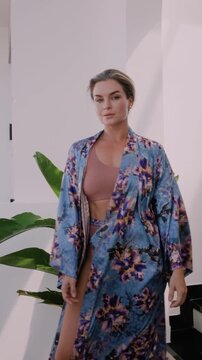 Elegant woman wearing luxury kimono robe over  swimsuit in modern tropical villa.