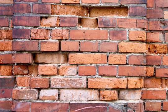 A wall made of bricks in various colors is seen in an urban setting. Some bricks are uneven, showing texture and age. The light touches the surface revealing details