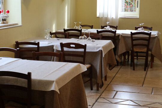 Sala interna di un ristorante rustico o trattoria tipica con tavoli apparecchiati con tovaglie beige e sedie in legno classico