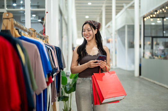 Young asian woman using smartphone while walking and shopping for clothes indoors