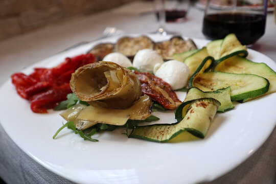 Piatto ricco di antipasto all'italiana con verdure grigliate, zucchine a nastro, melanzane, carciofi sott'olio, pomodori secchi e ciliegine di mozzarella fresca