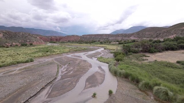 4K drone aerial view of La Poma, Salta, Argentina. Stunning Andean landscape with red rock mountains, green valleys and a river crossing the dramatic canyon scenery.