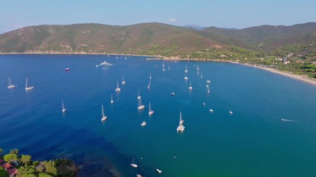 Aerial view of the yacht Netto II anchored in the crystal-clear waters of Lacona Bay, surrounded by the scenic coastline of Tuscany, Italy.