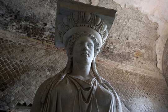 Inquadratura dal basso di una colonna a cariatide in marmo bianco raffigurante una figura femminile classica all'interno di un sito archeologico antico o museo