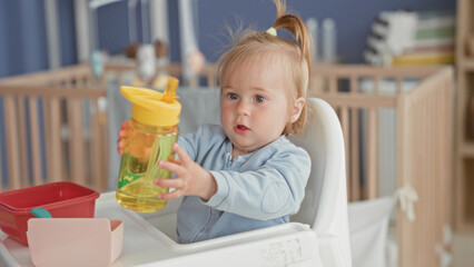 Toddler girl reaching for a yellow water bottle on a highchair tray in nursery  comfort feeding routine. © Krakenimages.com
