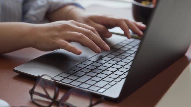 Young adult Caucasian woman typing on laptop keyboard, using trackpad, and working in modern office. Video is suitable for commercial use in corporate communication or remote work ads