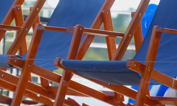 Blue seaside lounge chairs for relaxing with wooden frame in the Mediterranean city, touristic holiday boat 