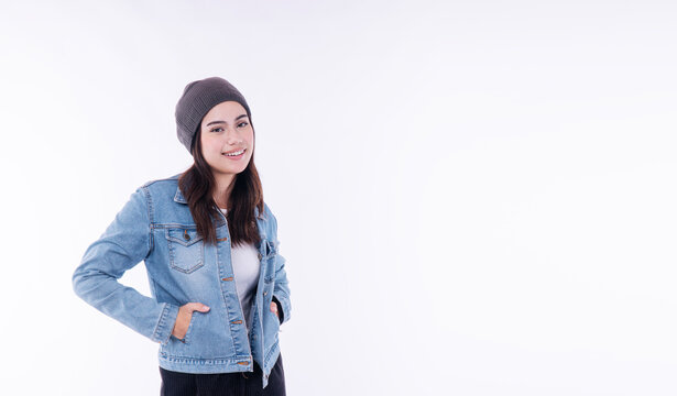 Portrait of beautiful smiling young Asian woman in casual blue denim jacket and beanie hat looking at camera on white background with copy space. Happy female student in winter fashion concept.