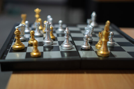 Close up of silver and gold chess pieces on a chessboard with shallow depth of field. Strategic planning, business competition, leadership, and intelligence concept.