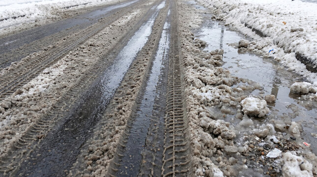 Car tire tracks in slush on muddy winter road  