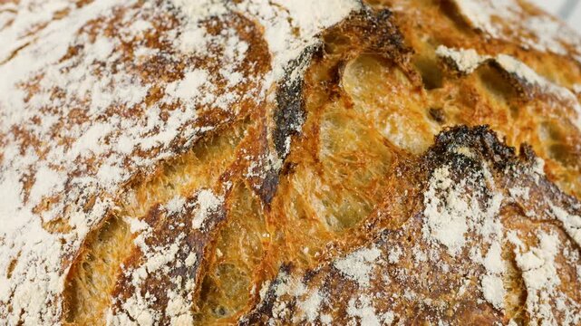 A close-up macro view of a freshly baked homemade sourdough wheat loaf with a crispy golden flour-dusted crust, spinning slowly to showcase its rustic artisan texture.