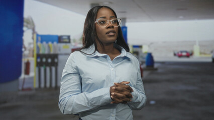 Woman adjusts shirt collar and gestures with hands beside a gas pump and canopy at a street fueling station  quiet confidence. © Krakenimages.com