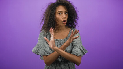 Obraz premium Curly haired woman with crossed hands signaling stop and bare hands visible in a purple studio; rejection refusal boundary.