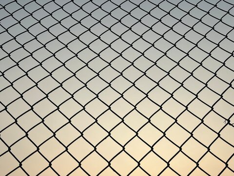 Silhouette of a chain link fence against a clear sky