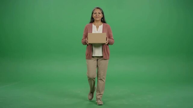 Smiling woman walking towards the camera holding a cardboard box, shot on a green screen.