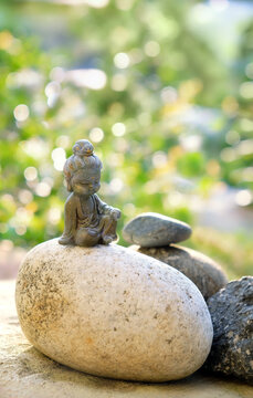 beautiful miniature Buddha figurine on stones close up outdoor, abstract natural background. landscape with cute little Buddhist monk figurine in garden. symbol of meditation, yoga. soft focus