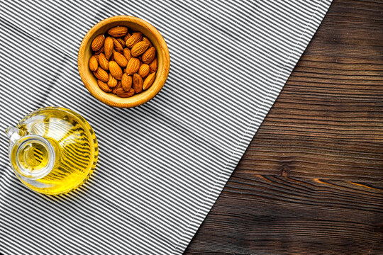 Oil for skin care. Almond oil near almond on dark wooden background top view copy space