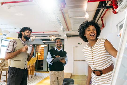 Diverse business professionals collaborating, smiling and writing on a whiteboard in a modern office setup. Concept of teamwork and discussion