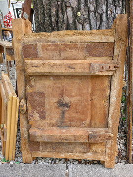 Weathered wooden cabinet door with rusty metal hinges placed outdoors next to a tree trunk in a garden setting