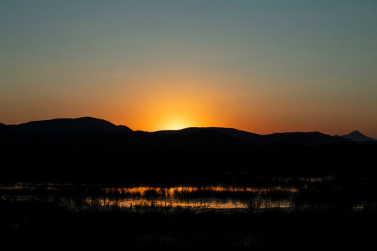 Sunset silhouette over rice fields in Pego Oliva Marjal National Park with mountains in the background
