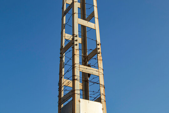Rustic metal lattice utility tower wrapped in barbed wire against blue sky