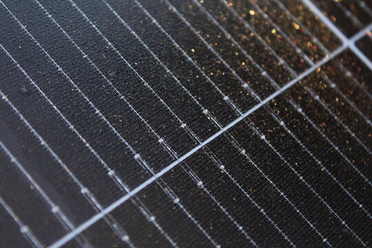 Macro view of a solar panel surface covered in morning dew droplets reflecting warm golden sunlight in a textured, diagonal composition.