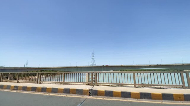 Motorcycle Ride Across Bridge Over Indus River in Khyber Pakhtunkhwa,  The footage shows the road, bridge railing, river and surrounding landscape from the side while traveling. 