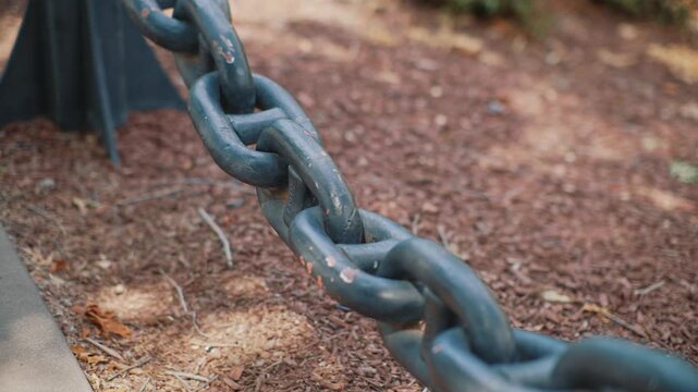 Close up view of massive metal chain in park shows strong interconnected links with selective focus and metal surface texture in an outdoor environment