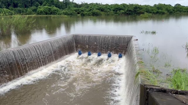 A concrete weir structure controls water flow in a rural river. The storage system features blue valves releasing stream current during irrigation supply management for agriculture.
