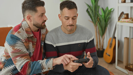 Two men on bed playing with a game controller, one guides hand on controller and both hold joystick in a building room  intimacy bonding. © Krakenimages.com