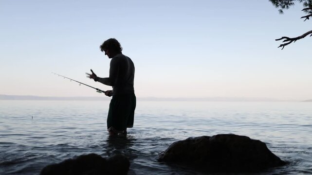 Young angler looks disappointed while standing in shallow sea water because fish are not biting and a new unsuccessful fishing attempt ends without any catch this evening