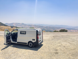 A white camper van parked at a mountain overlook with its door open, evoking the concepts of road trips, freedom, a nomadic lifestyle, and tourism on wheels. © Paolo Corazza