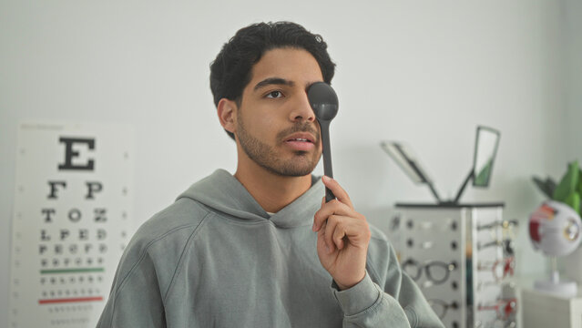 Man holding an eye occluder over one eye and making thumb and pointing gestures in an optometry clinic building; concentration vision care.